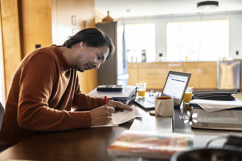 父亲在厨房的餐桌上使用笔记本电脑并支付账单图片素材