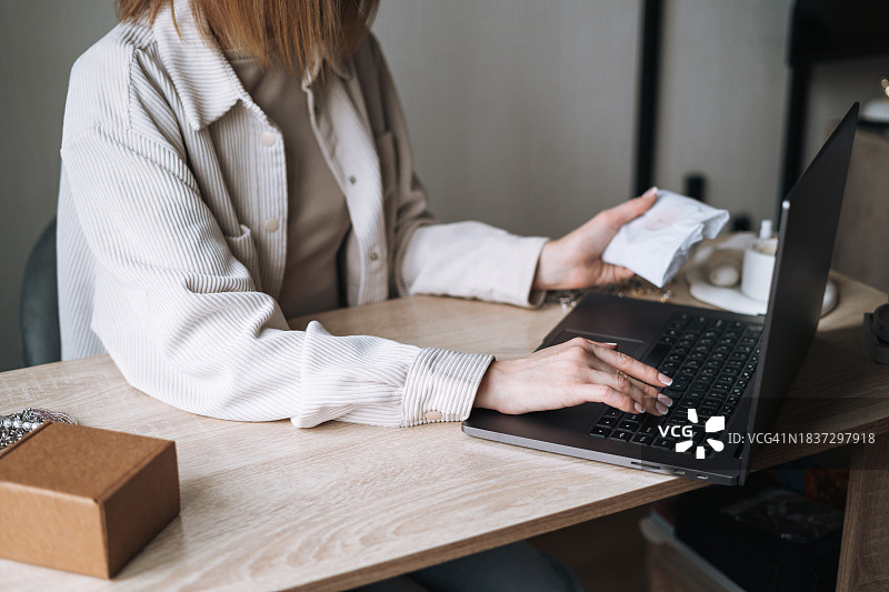 小型企业主，珠宝设计师收集和包装网上订单，在工作室的桌子上使用笔记本电脑工作图片素材