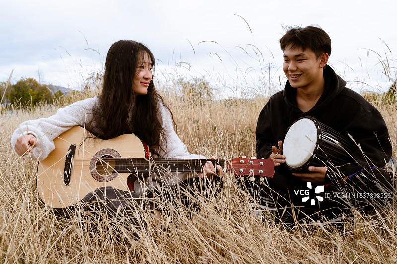 两个年轻男人坐在草地上演奏乐器图片素材