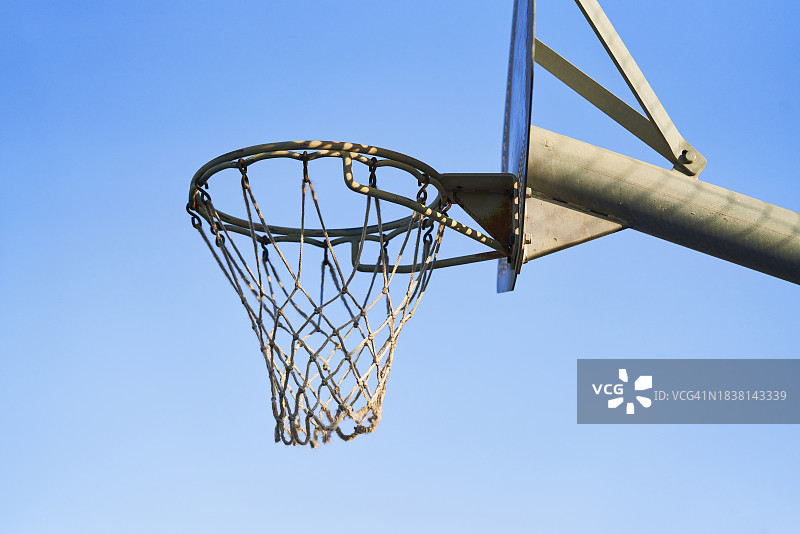 侧视视角：户外篮球场篮板上的网状篮筐，天空为背景图片素材