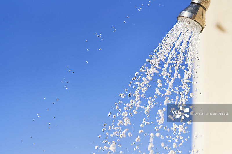 从室外金属喷壶流出的水流，天空为背景的正面图图片素材