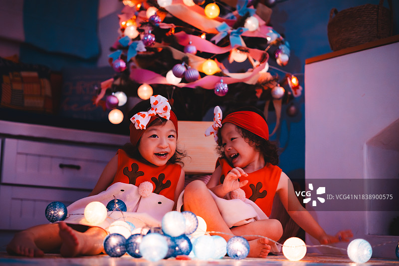 双倍的快乐：圣诞树旁穿着驯鹿服装的双胞胎女婴图片素材