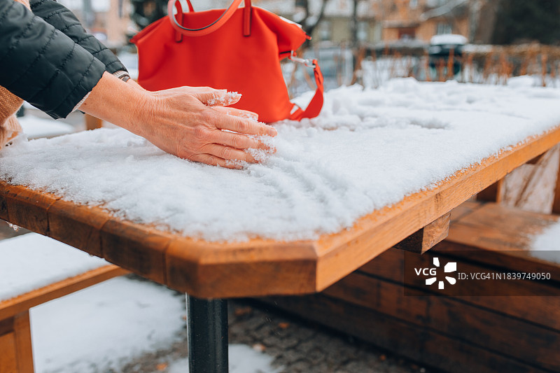 女子轻抚被白雪覆盖的户外木桌，享受生活中的简单乐趣图片素材