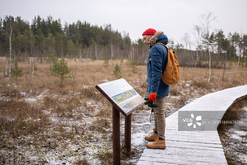 男子在松树林信息栏旁阅读休息图片素材