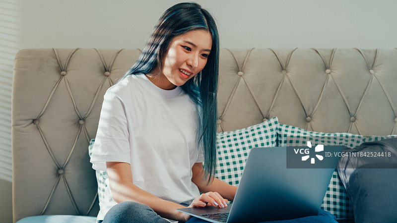 忙碌的亚洲年轻女人坐在床上用电脑笔记本拿着文书，看着凌乱的文件，思考早上在卧室里检查工作。保持隔离，在家工作。图片素材