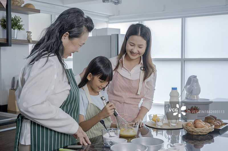 快乐的三代女性烹饪手工糕点，揉捏、擀面，在厨房里，快乐的小女孩与微笑的母亲和成熟的祖母一起享受居家休闲时光图片素材