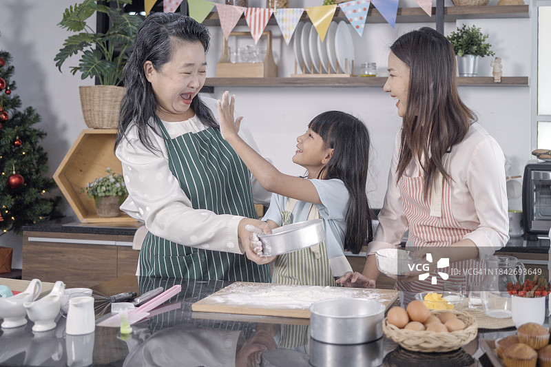 快乐的三代女性烹饪手工糕点，揉捏、擀面，在厨房里，快乐的小女孩与微笑的母亲和成熟的祖母一起享受居家休闲时光图片素材