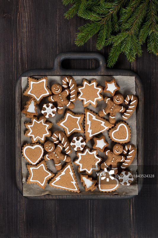 用糖霜装饰的节日姜饼。圣诞树、星星、雪花、带拐杖的姜饼人、心形。在木盘上。深色木制背景。用树枝装饰。俯视图。圣诞节。新年图片素材