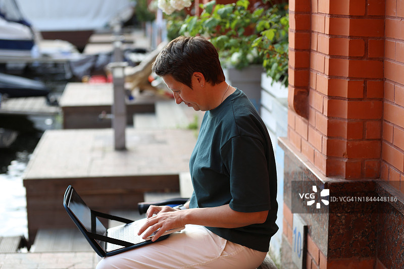 在河岸咖啡馆用笔记本电脑工作的中年自由职业女性，看着设备屏幕图片素材