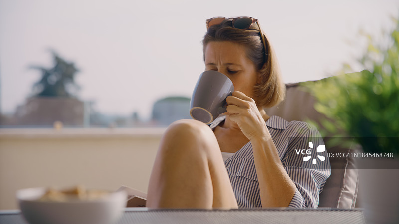 放松的中年妇女坐在露台椅子上喝咖啡图片素材