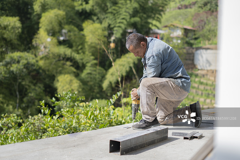 一位拉丁裔工人在阳台施工中使用钻头破拆地板图片素材