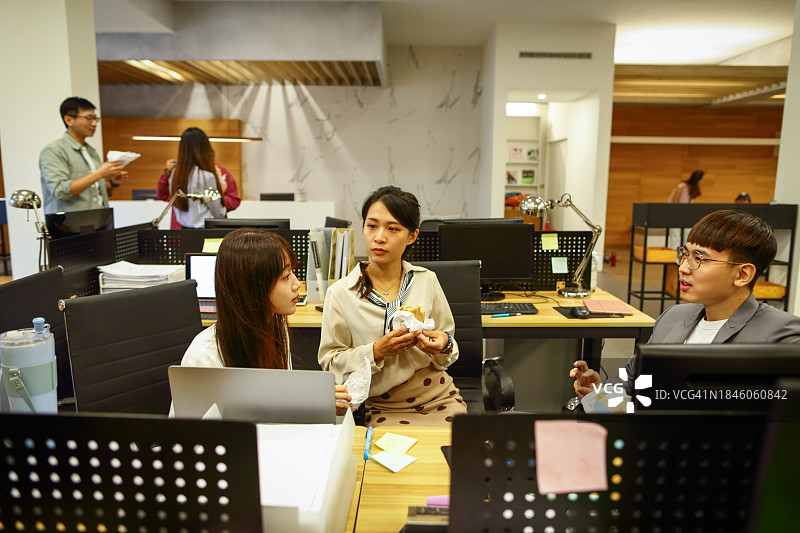 手拿外卖午餐的亚洲商人在办公室利用午餐时间继续交流讨论图片素材