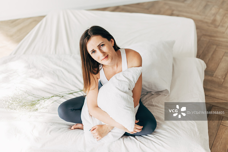 年轻女人在舒适的床上拥抱枕头，床上有丝滑的亚麻布图片素材