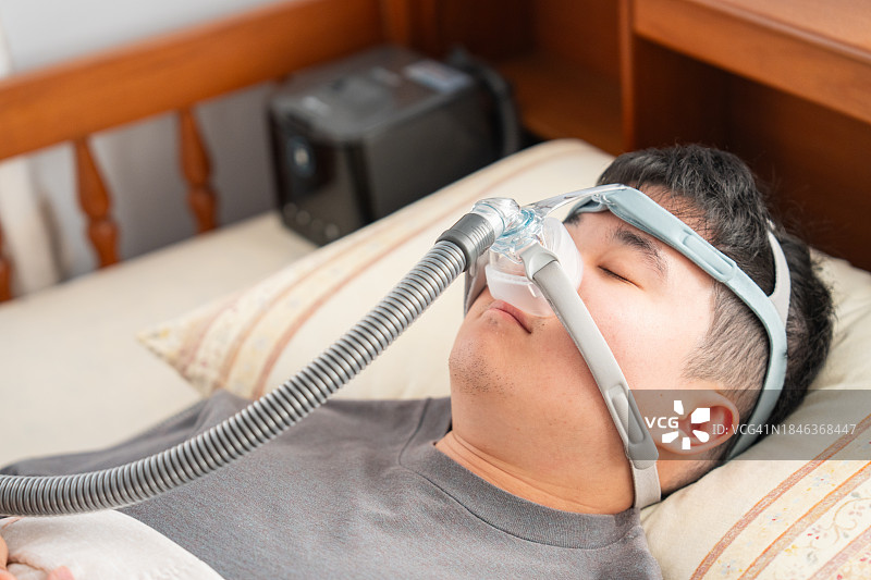 患有阻塞性睡眠呼吸暂停的男子戴着CPAP面罩睡觉图片素材