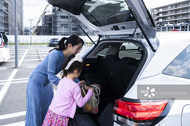 年轻母亲和女儿在停车场购物后将食品放入后备箱图片素材
