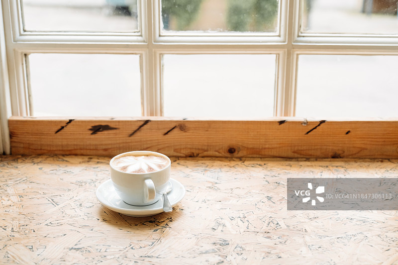 咖啡店靠窗木桌上的陶瓷杯卡布奇诺图片素材