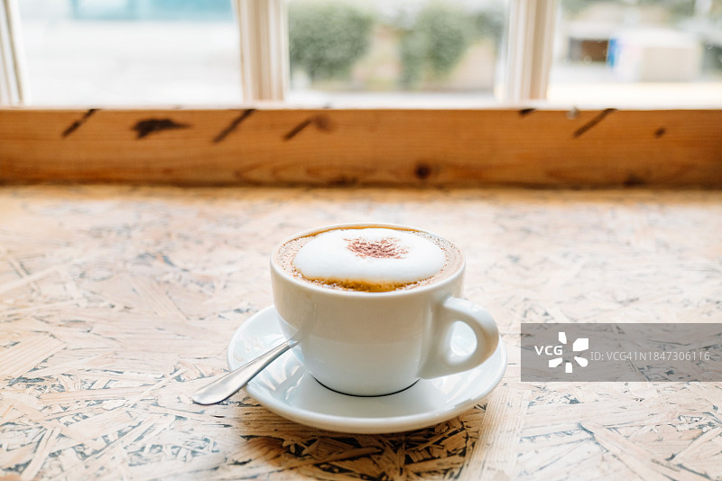 咖啡店靠窗木桌上的陶瓷杯卡布奇诺图片素材