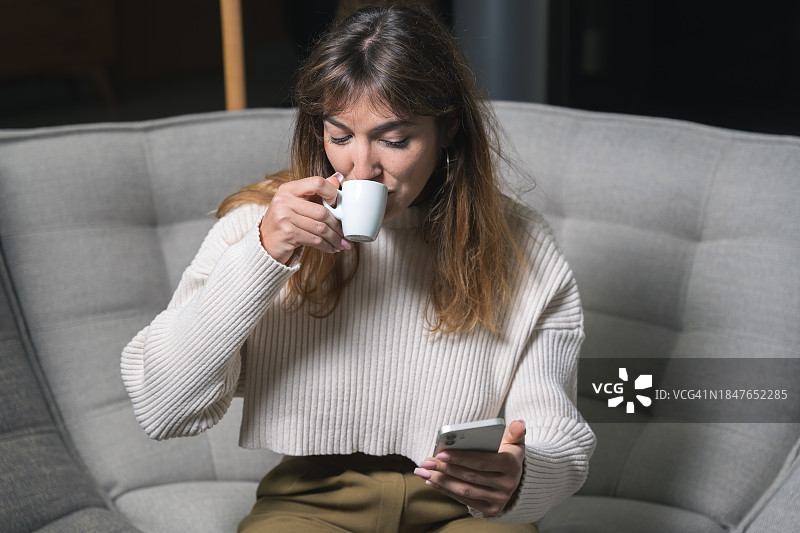 年轻女人坐在现代沙发上使用智能手机图片素材