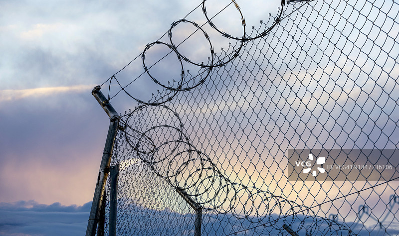日落时分带刺铁丝网的金属围栏特写图片素材