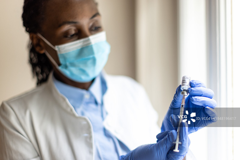 戴着手套的黑人护士拿着装有COVID-19疫苗的安瓿瓶和注射器图片素材