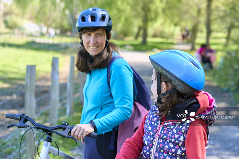 女人和女孩互相看着，戴着防护头盔，女人笑着拿着自行车图片素材
