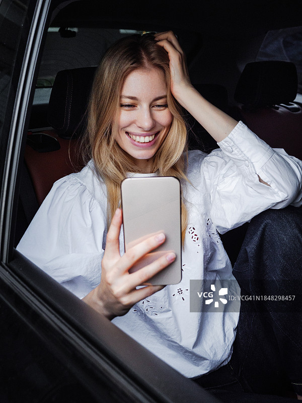 年轻金发女孩坐在车里愉快地和朋友通电话图片素材