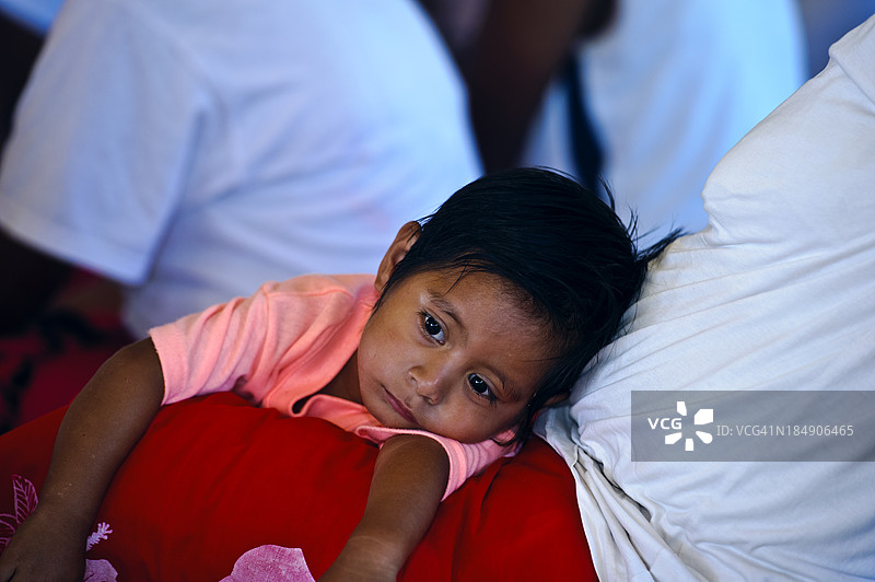 一个小男孩在村庄仪式上依偎在母亲的怀里。图片素材