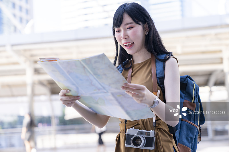 快乐的年轻亚洲女性正在看地图，计划城市旅行图片素材