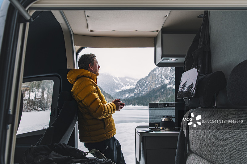成熟男子在冬季的法国阿尔卑斯山停放的露营车中的侧视图图片素材