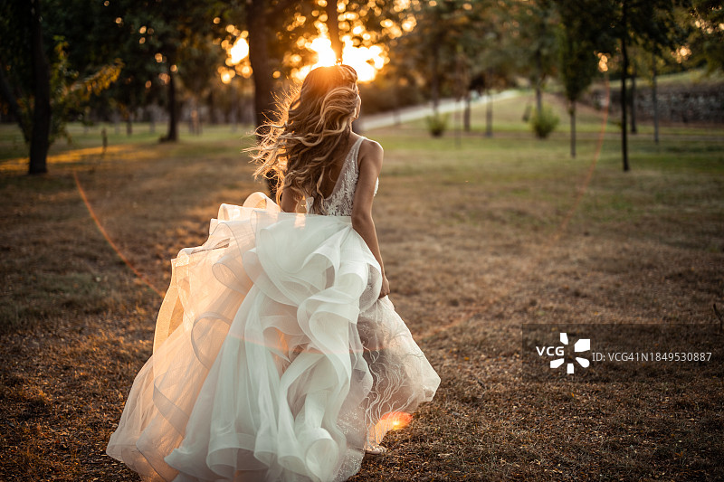 日落时分，新娘在公园草坪上奔跑（背影）图片素材