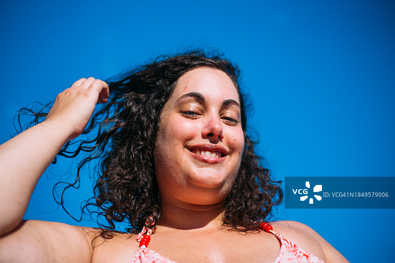 在蓝色背景下抚摸卷发的丰满女子图片素材