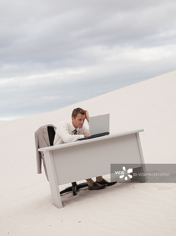 商人坐在沙漠中间的桌子旁，使用笔记本电脑图片素材