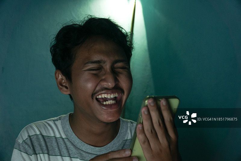 观看手机短剧时大笑的年轻男子图片素材