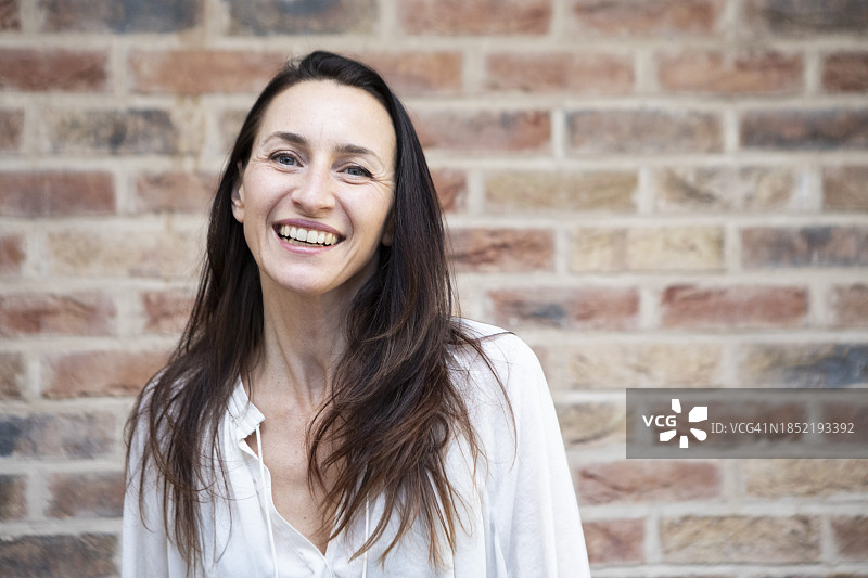 快乐的女人站在砖墙旁图片素材