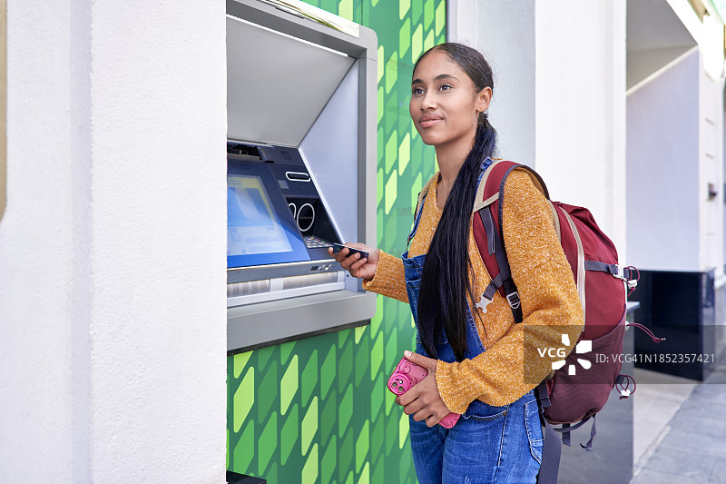 年轻漂亮的哥伦比亚拉丁裔数码游民女孩，背着背包在ATM机上用信用卡扫描图片素材