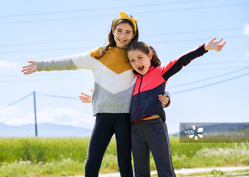 小女孩们拥抱微笑看向镜头：户外可爱女孩与美丽风景图片素材