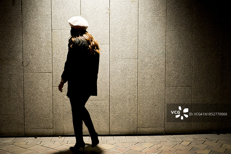 一位穿着夹克和帽子，站在灯笼下的美丽女人的背影图片素材