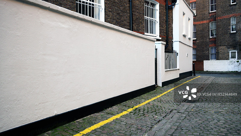 干净的白色墙壁，鹅卵石街道和风化的砖砌外墙，位于英国伦敦图片素材