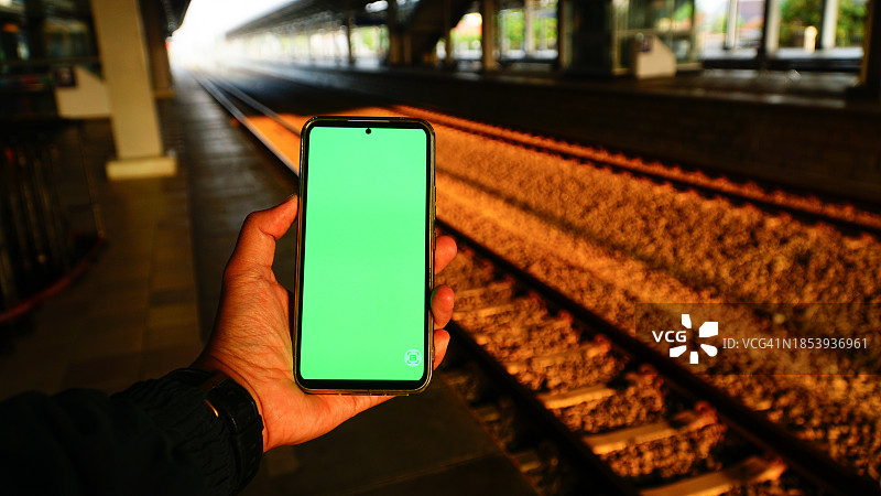在早晨的火车站背景中使用带绿屏的智能手机图片素材