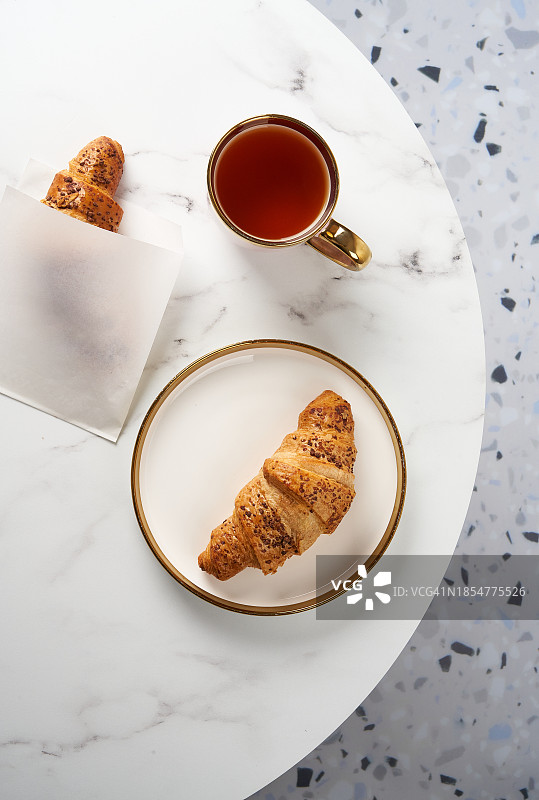 两个美味的羊角面包、盘子和热饮在咖啡馆的圆桌上图片素材