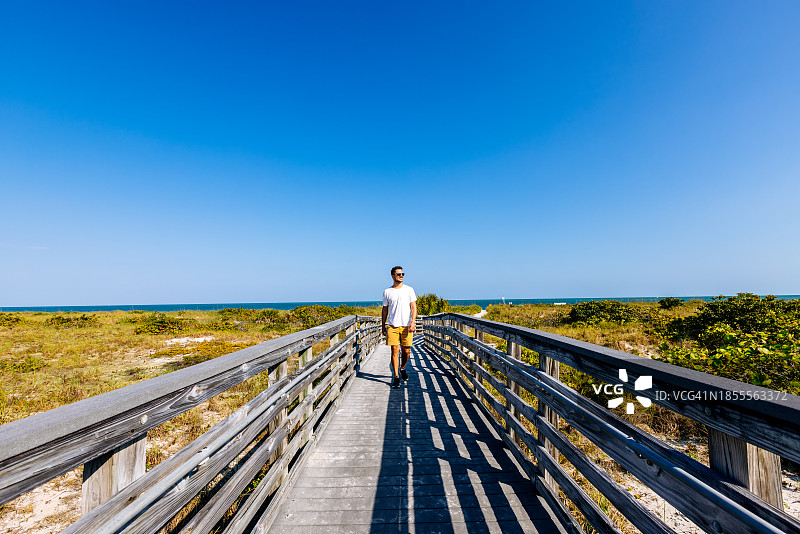 在美国佛罗里达州比尔·巴格斯海角佛罗里达州立公园木板路上戴太阳镜的快乐男人行走图片素材