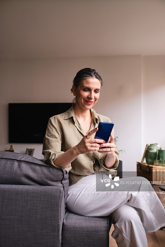 坐在沙发上使用手机的休闲商务女士图片素材