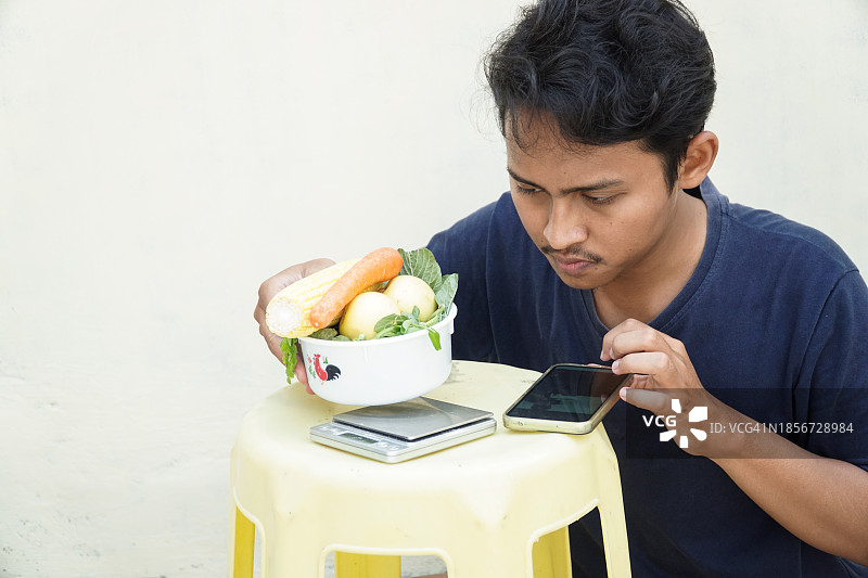 用电子秤称重蔬菜的年轻男人图片素材