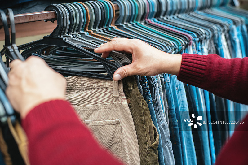 男子在跳蚤市场挑选二手衣服：可持续生活方式、旧货交易和升级改造概念图片素材