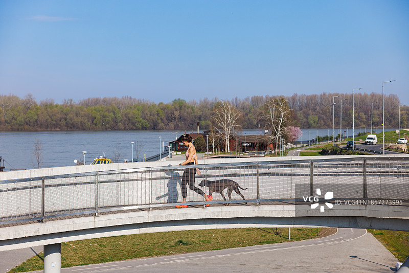 在城市海滨空旷的高架走道上和她的狗一起奔跑图片素材