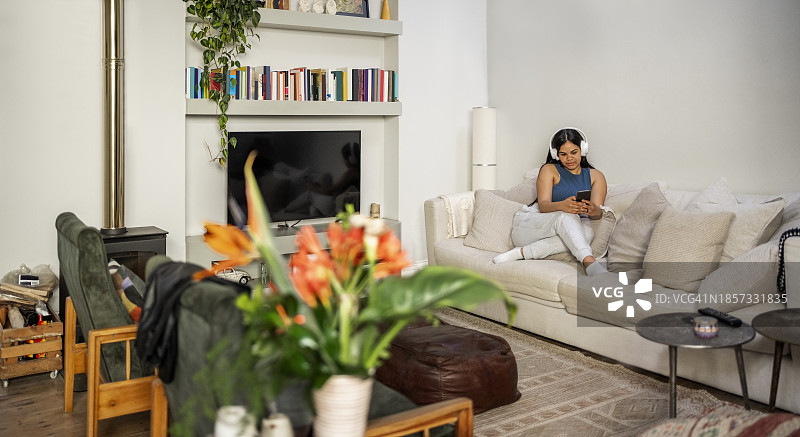 年轻女人在家坐在沙发上用手机和耳机听音乐图片素材