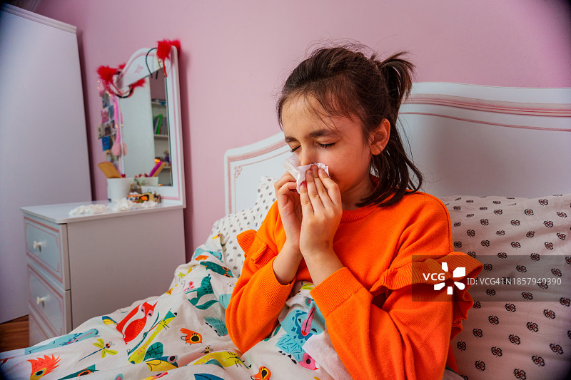 悲伤的孩子坐在床上用白色餐巾纸擤鼻涕图片素材
