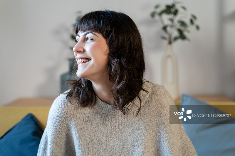 一位微笑的年轻女子坐在家里的沙发上的肖像图片素材