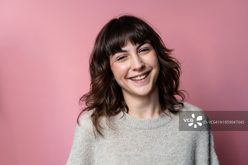 粉色背景中穿着毛衣的微笑女性肖像图片素材