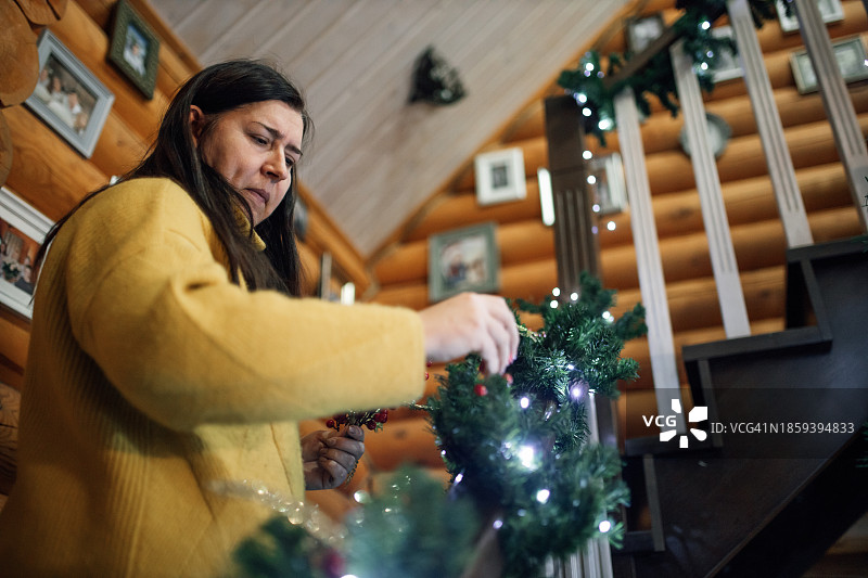 迷人的家庭主妇用圣诞装饰元素精心装饰楼梯栏杆的低角度视图图片素材